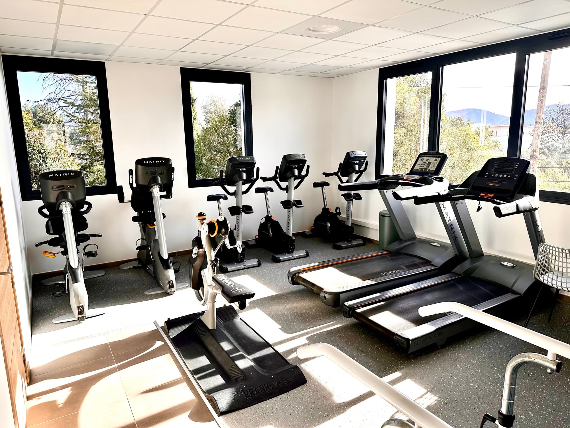 Salle de réentraînement à l'effort avec vélos et tapis de course, baignée de lumière